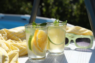 Photo of Tasty cocktail in glasses and sunglasses near swimming pool outdoors