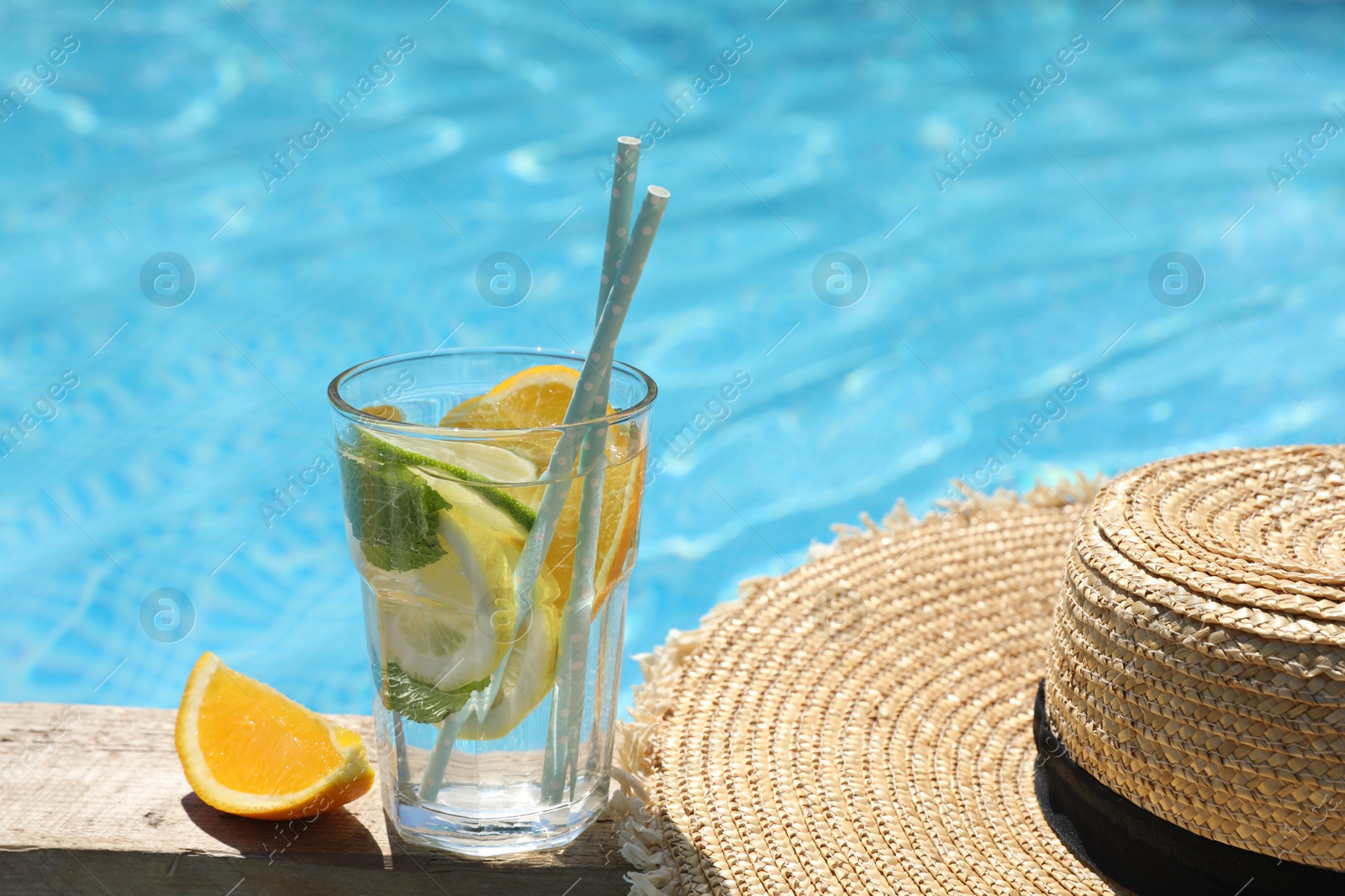 Photo of Tasty cocktail in glass and straw hat near swimming pool outdoors