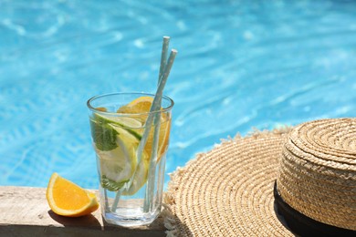 Photo of Tasty cocktail in glass and straw hat near swimming pool outdoors