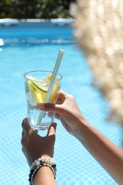 Photo of Woman holding tasty cocktail in glass near swimming pool outdoors, closeup