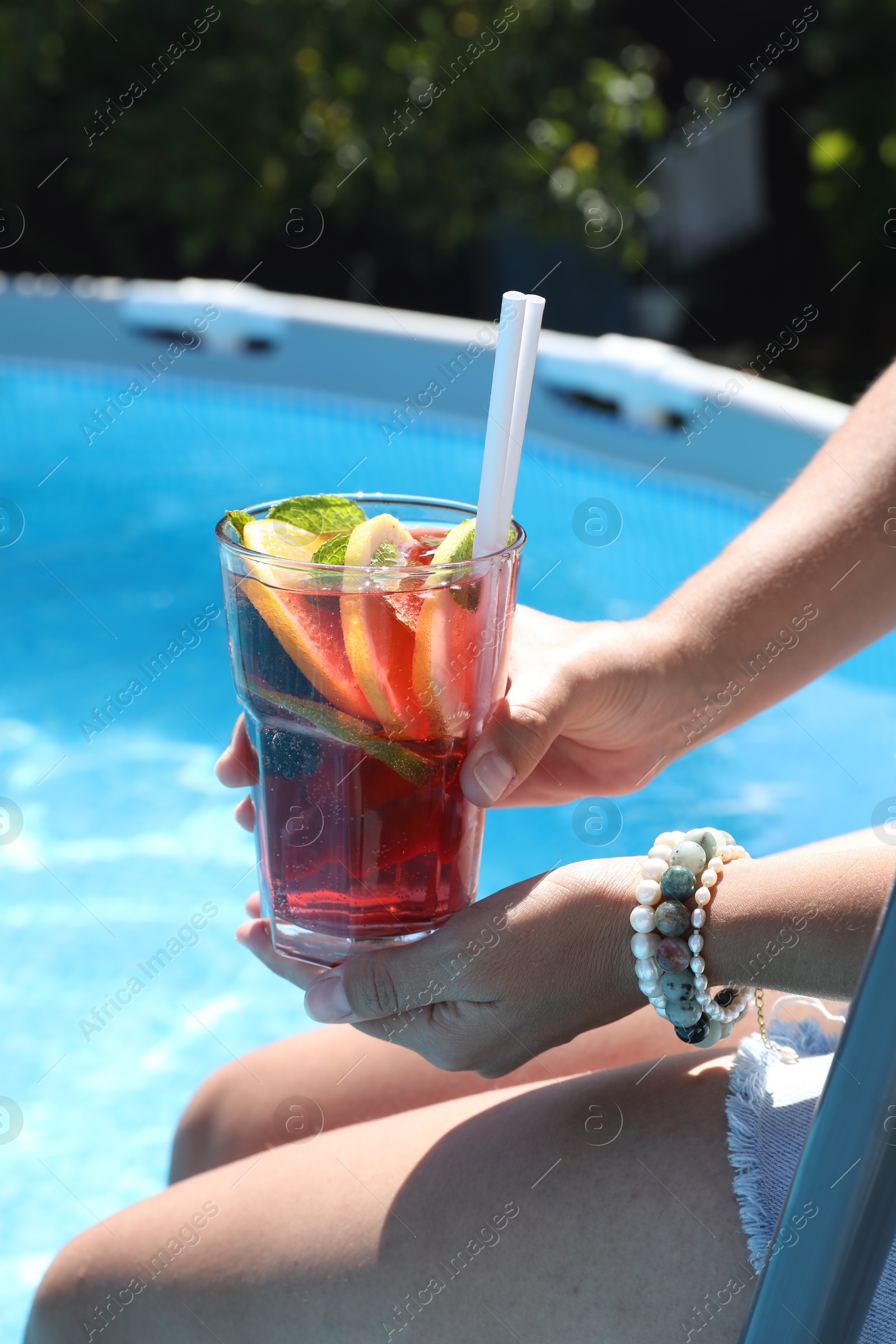 Photo of Woman holding tasty cocktail in glass near swimming pool outdoors, closeup