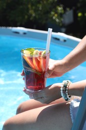 Woman holding tasty cocktail in glass near swimming pool outdoors, closeup