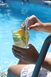 Photo of Woman holding tasty cocktail in glass near swimming pool outdoors, closeup