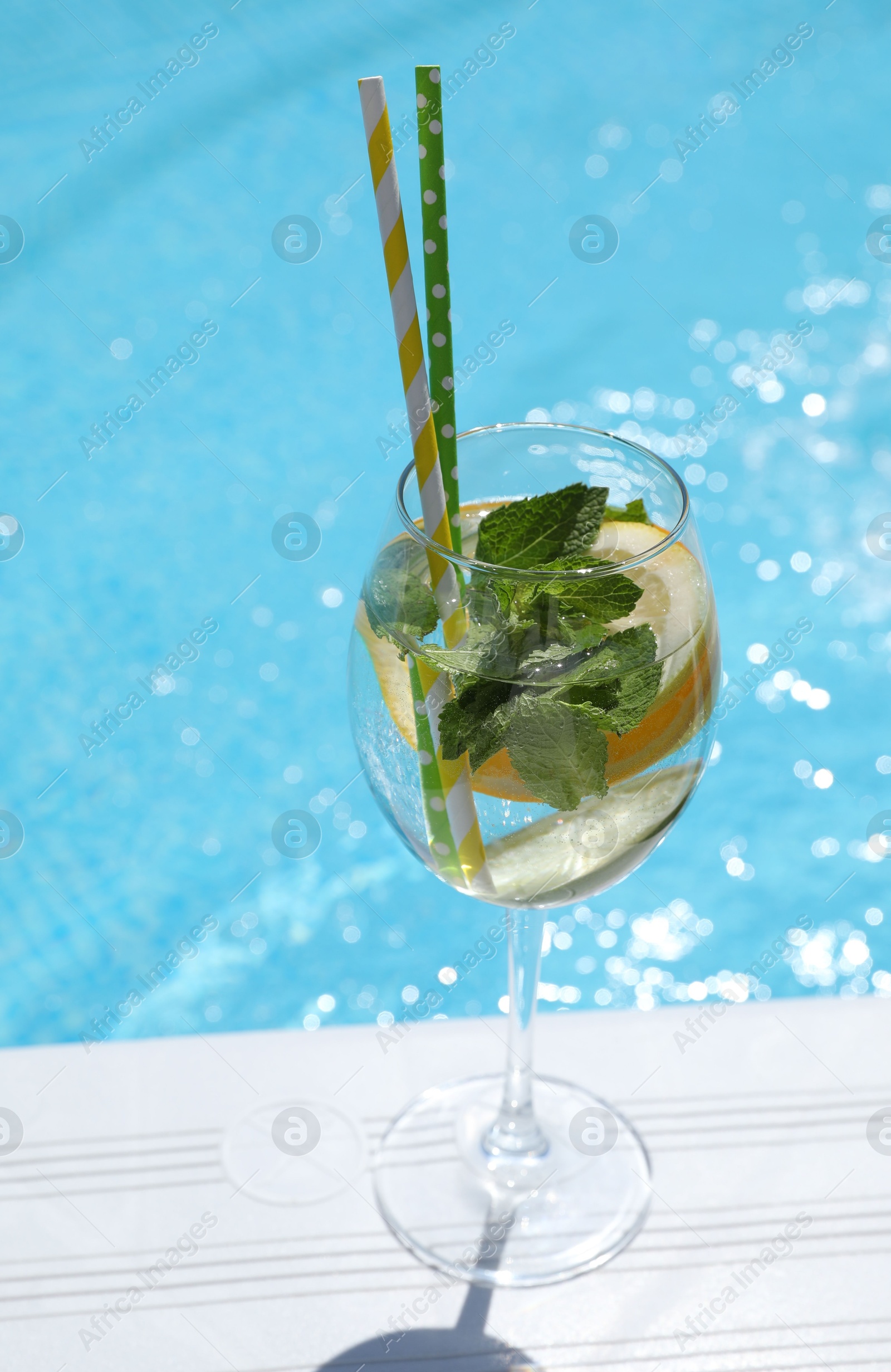 Photo of Tasty cocktail in glass near swimming pool outdoors