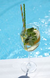 Photo of Tasty cocktail in glass near swimming pool outdoors