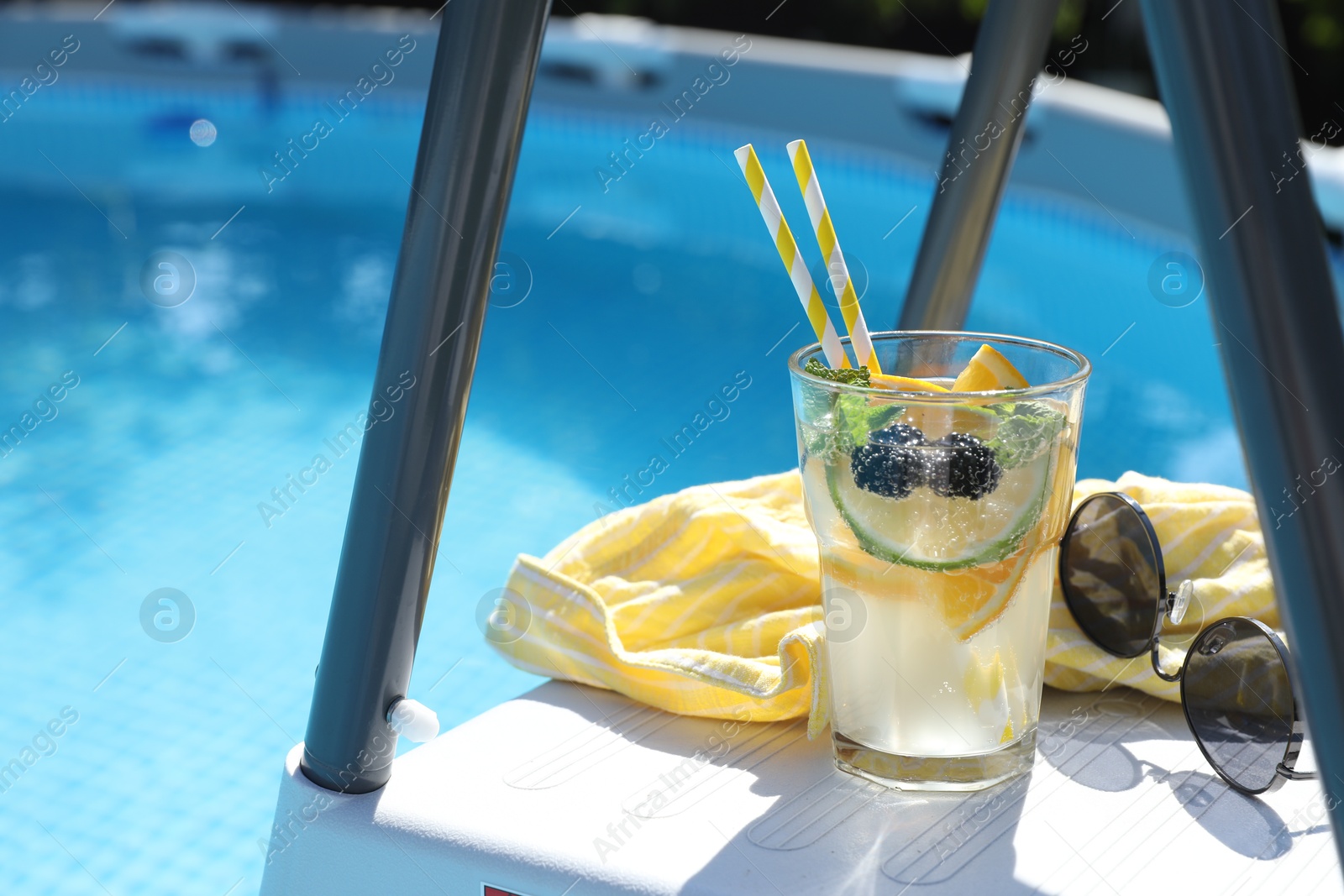 Photo of Tasty cocktail in glass near swimming pool outdoors, space for text