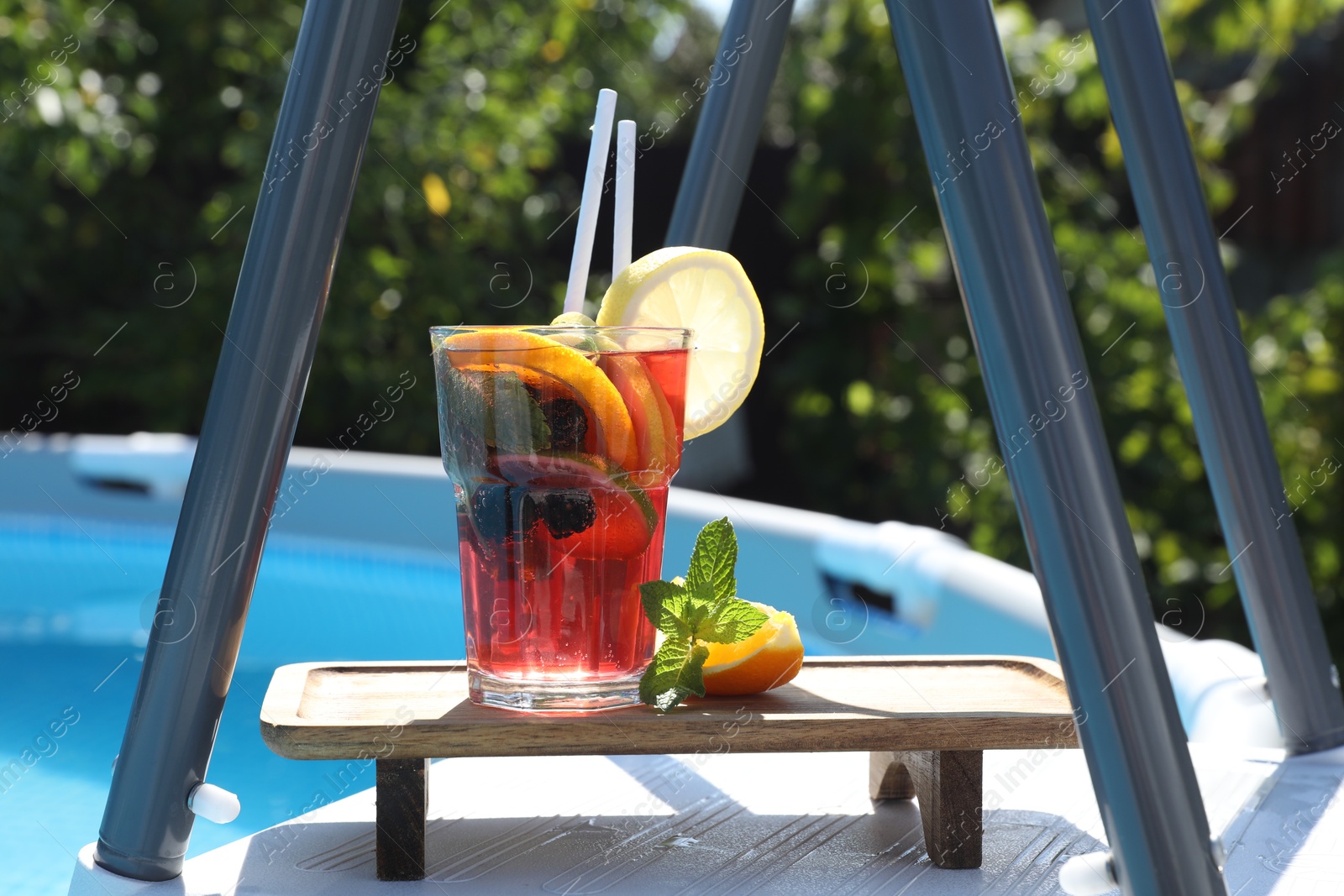 Photo of Tasty cocktail in glass near swimming pool outdoors