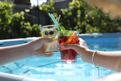 Photo of Women holding tasty cocktail in glass near swimming pool outdoors, closeup