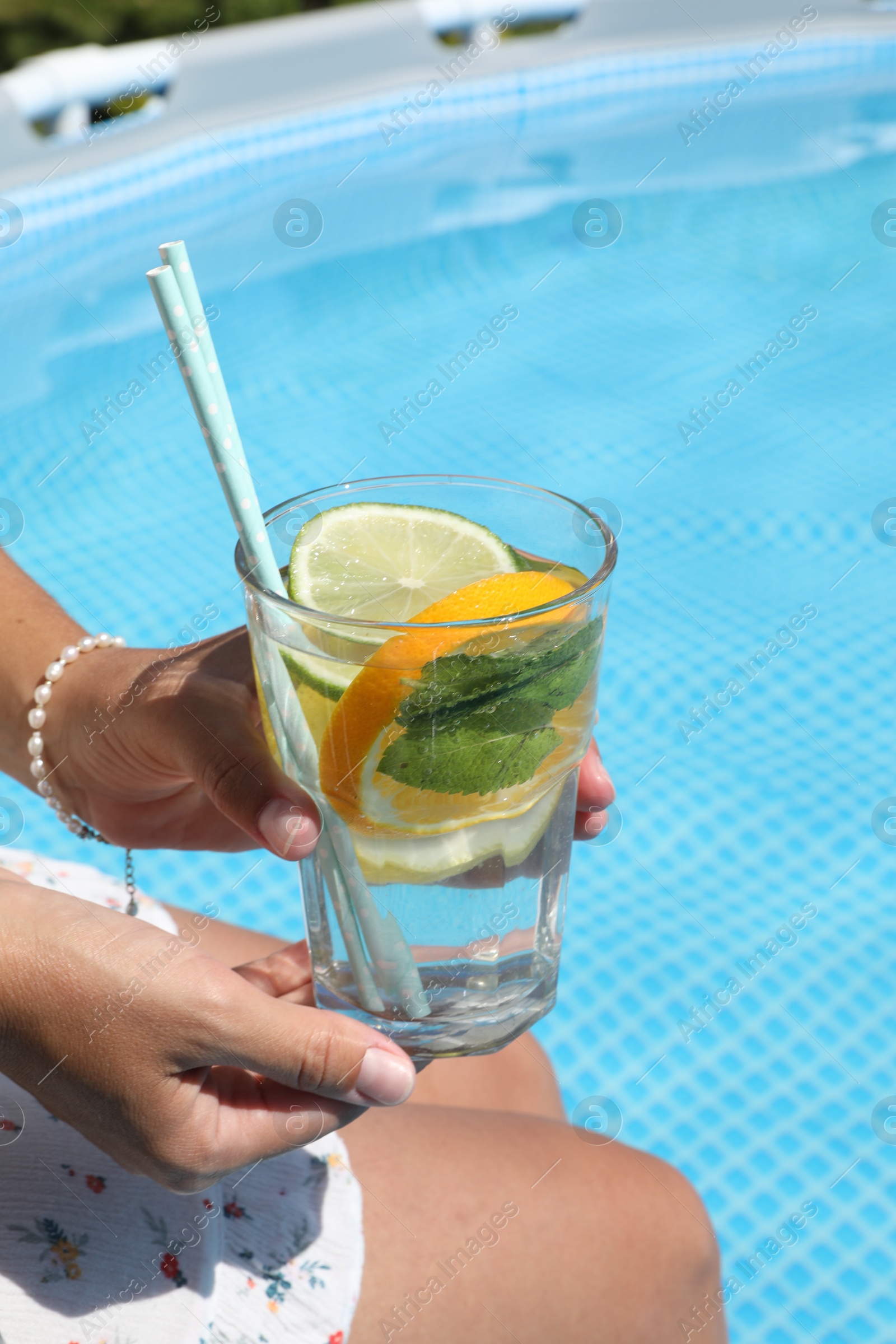 Photo of Woman holding tasty cocktail in glass near swimming pool outdoors, closeup