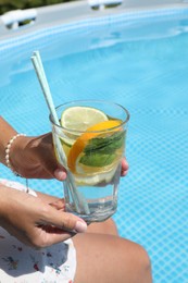 Photo of Woman holding tasty cocktail in glass near swimming pool outdoors, closeup