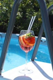 Photo of Tasty cocktail in glass near swimming pool outdoors