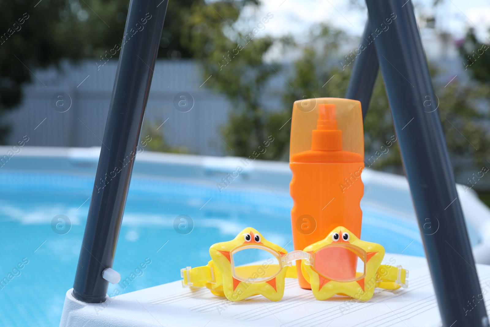 Photo of Bottle of sunscreen and swim goggles near swimming pool outdoors