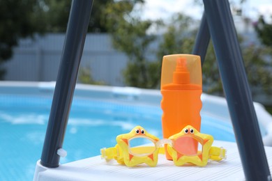 Photo of Bottle of sunscreen and swim goggles near swimming pool outdoors