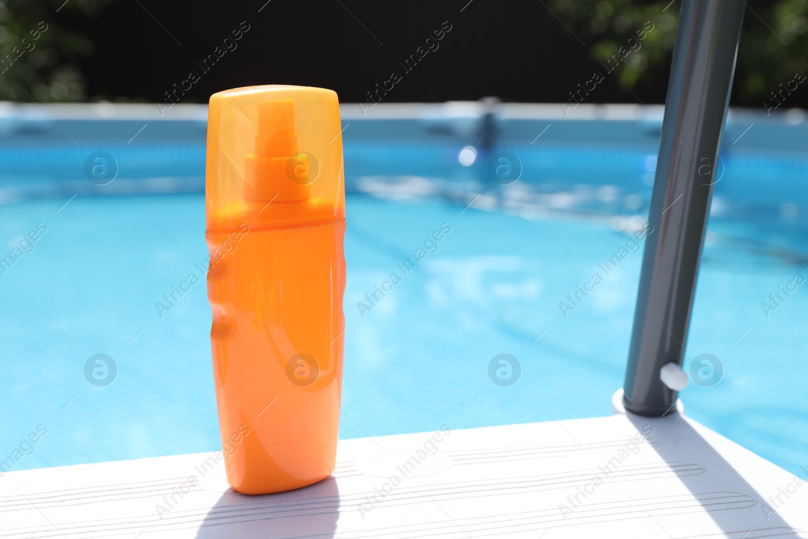 Photo of Bottle of sunscreen near swimming pool outdoors, space for text