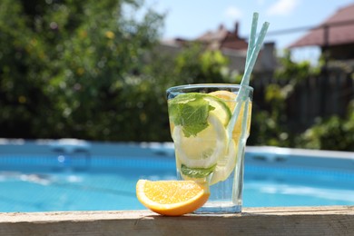 Photo of Tasty cocktail in glass near swimming pool outdoors