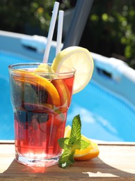 Photo of Tasty cocktail in glass near swimming pool outdoors