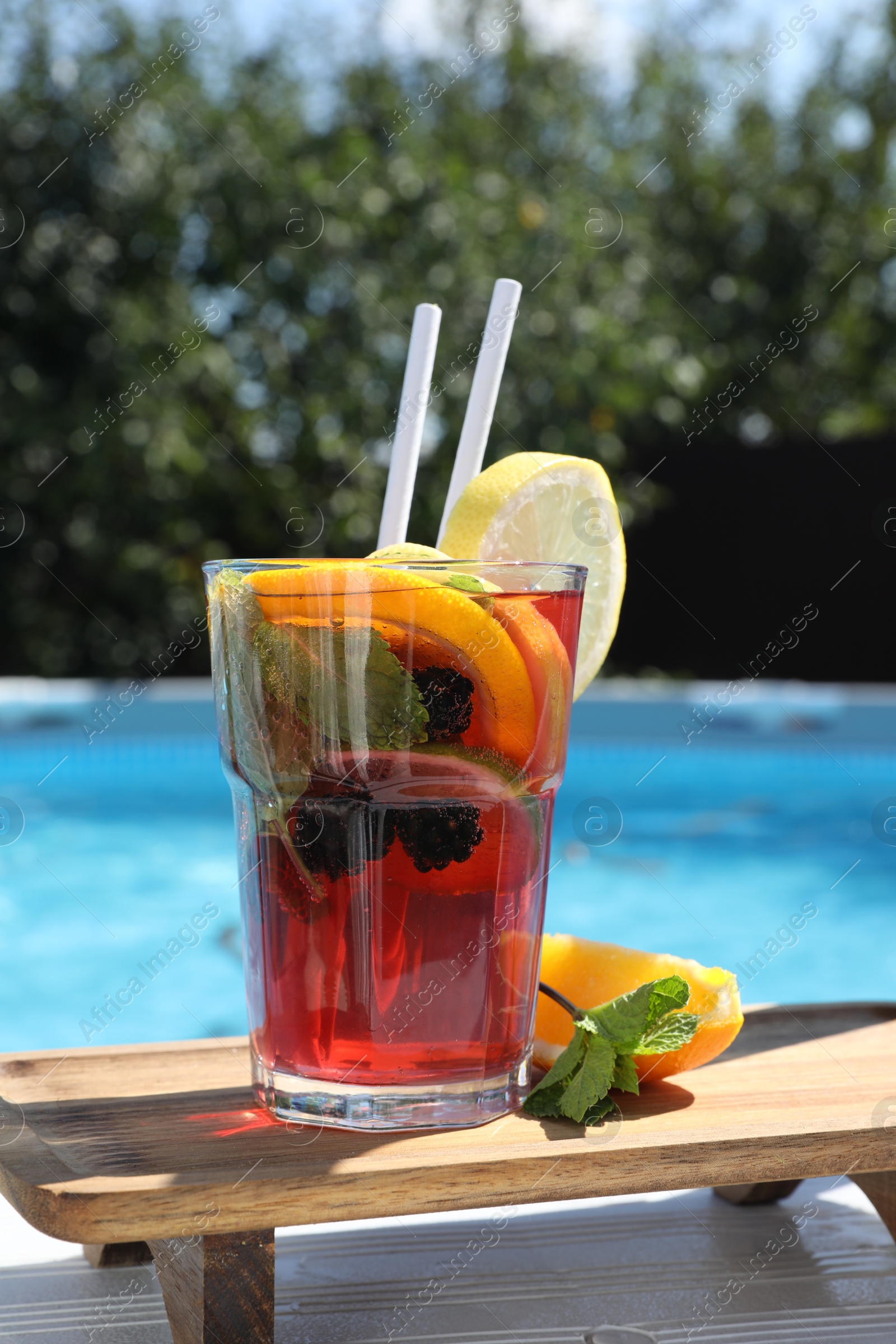 Photo of Tasty cocktail in glass near swimming pool outdoors