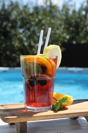 Photo of Tasty cocktail in glass near swimming pool outdoors