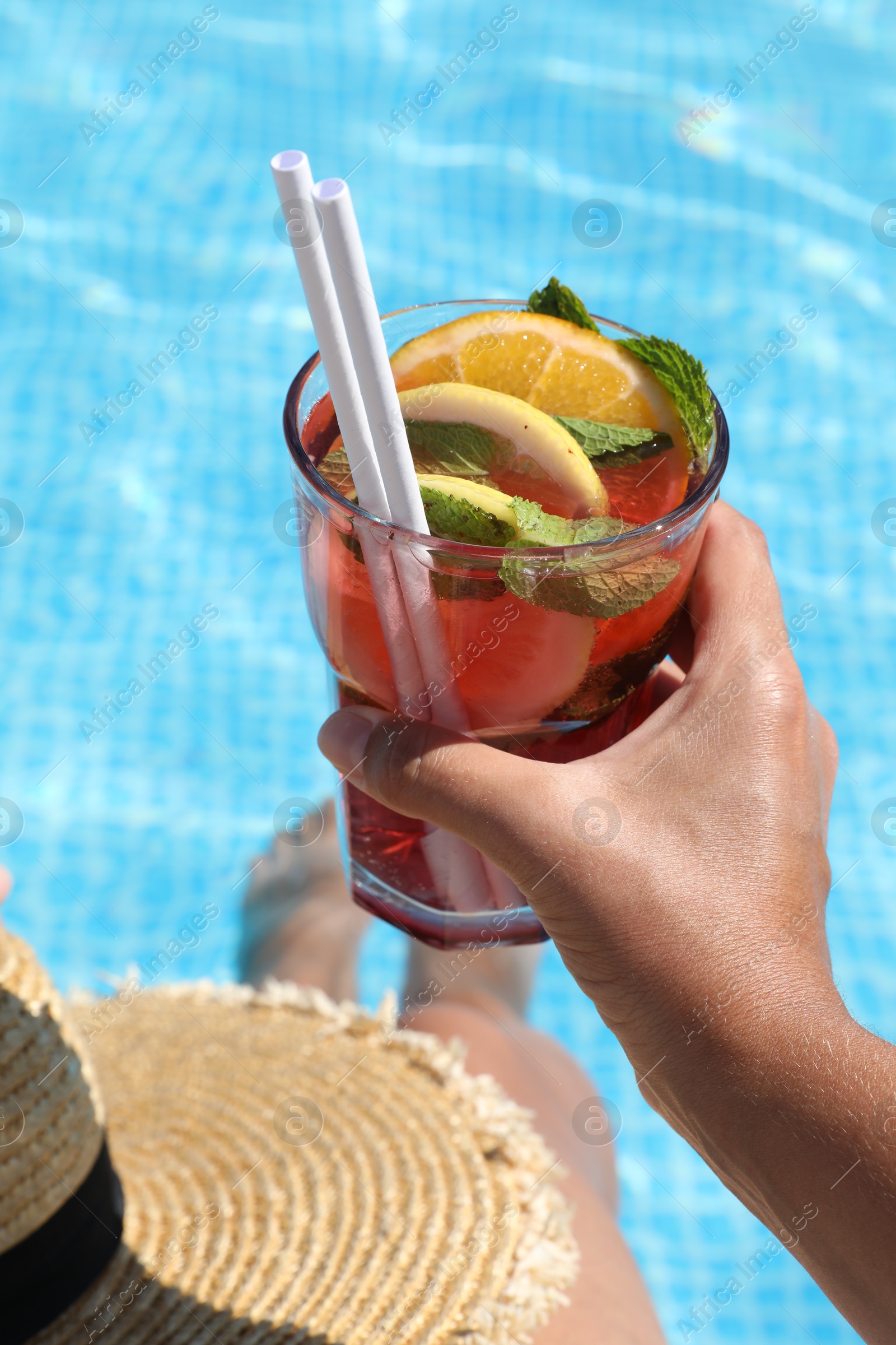 Photo of Woman holding tasty cocktail in glass near swimming pool outdoors, closeup