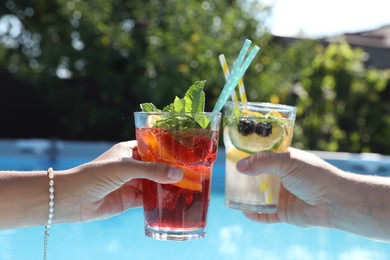 Photo of Women holding tasty cocktail in glass near swimming pool outdoors, closeup