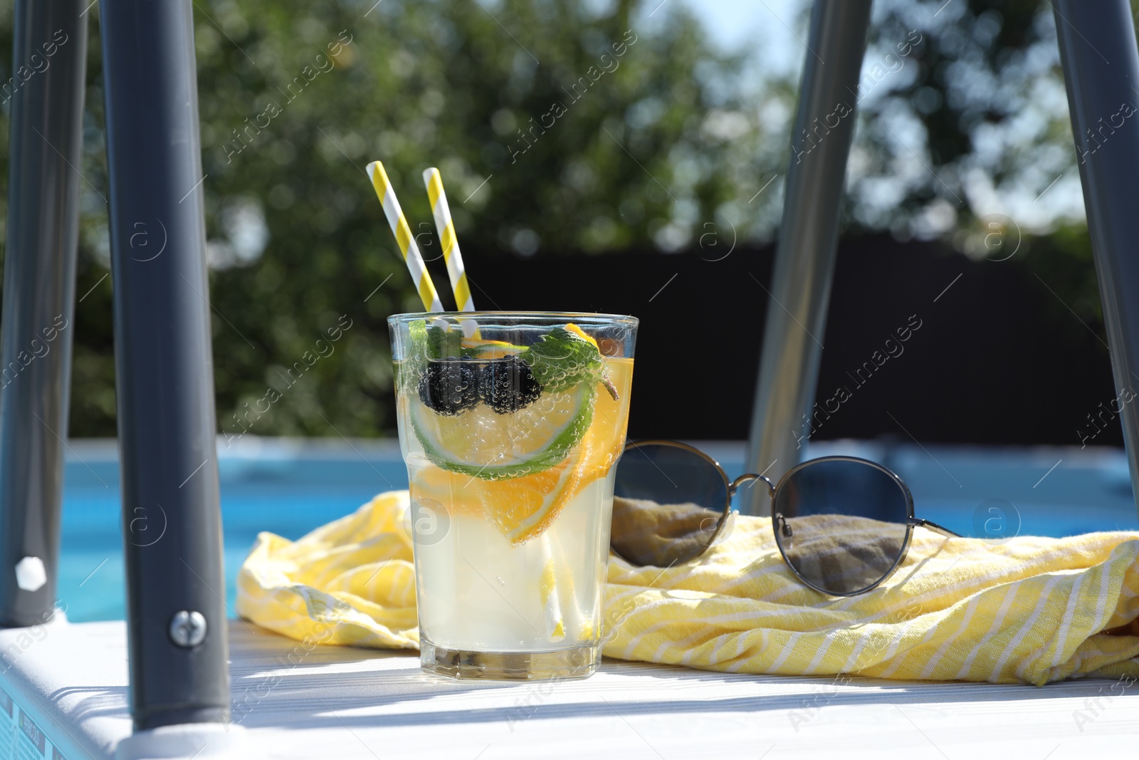 Photo of Tasty cocktail in glass and sunglasses near swimming pool outdoors