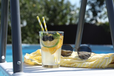 Photo of Tasty cocktail in glass and sunglasses near swimming pool outdoors