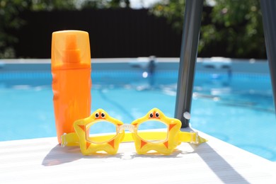 Photo of Bottle of sunscreen and swim goggles near swimming pool outdoors