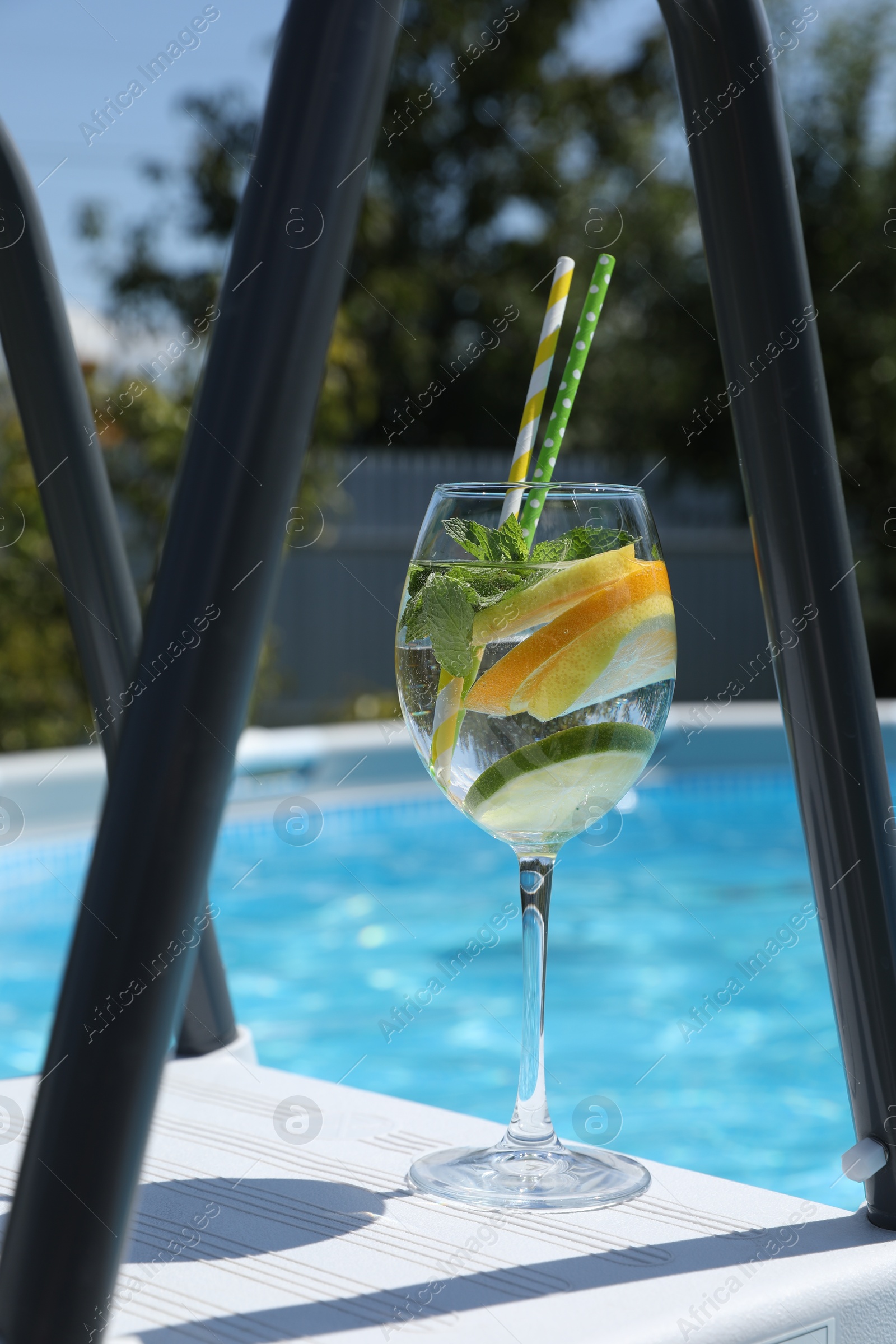 Photo of Tasty cocktail in glass near swimming pool outdoors