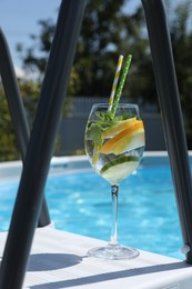 Photo of Tasty cocktail in glass near swimming pool outdoors