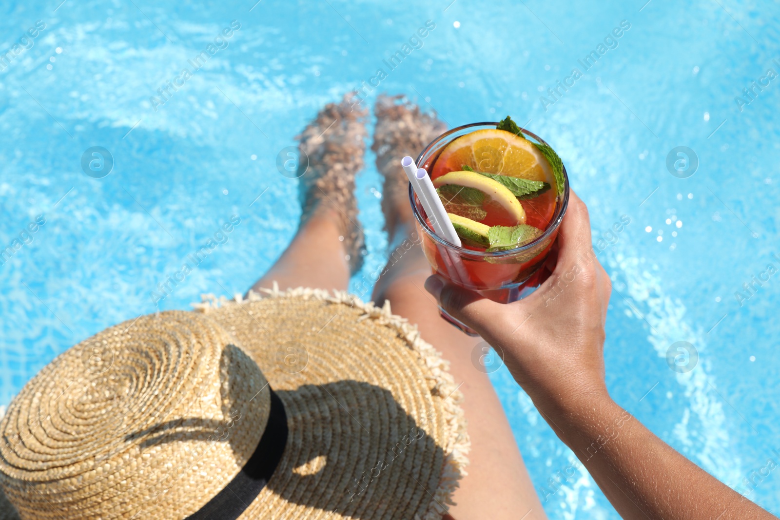 Photo of Woman holding tasty cocktail in glass near swimming pool outdoors, closeup