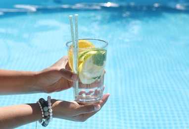 Photo of Woman holding tasty cocktail in glass near swimming pool outdoors, closeup