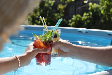 Women holding tasty cocktail in glass near swimming pool outdoors, closeup