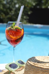 Photo of Tasty cocktail in glass and straw hat near swimming pool outdoors