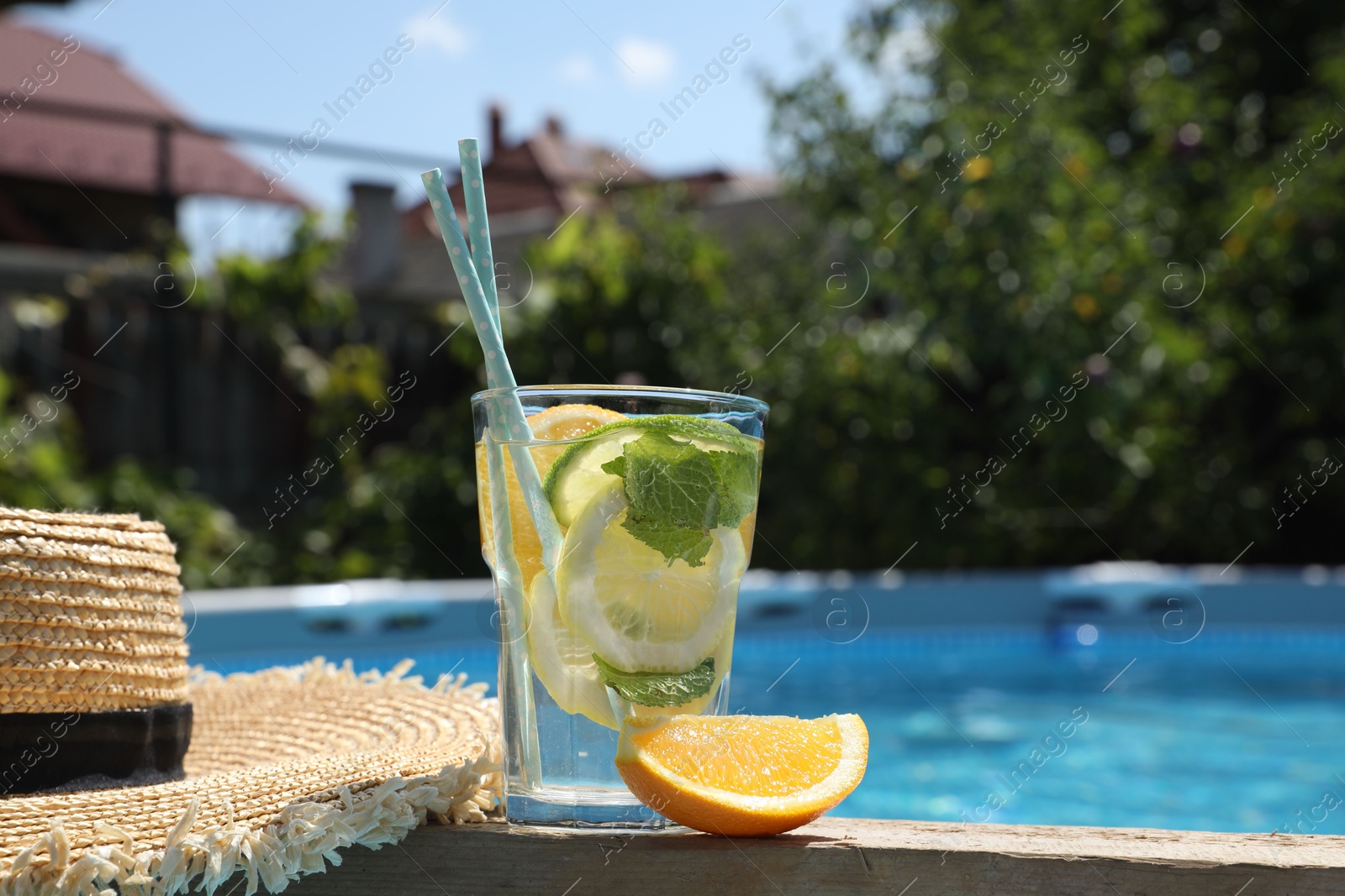 Photo of Tasty cocktail in glass and straw hat near swimming pool outdoors