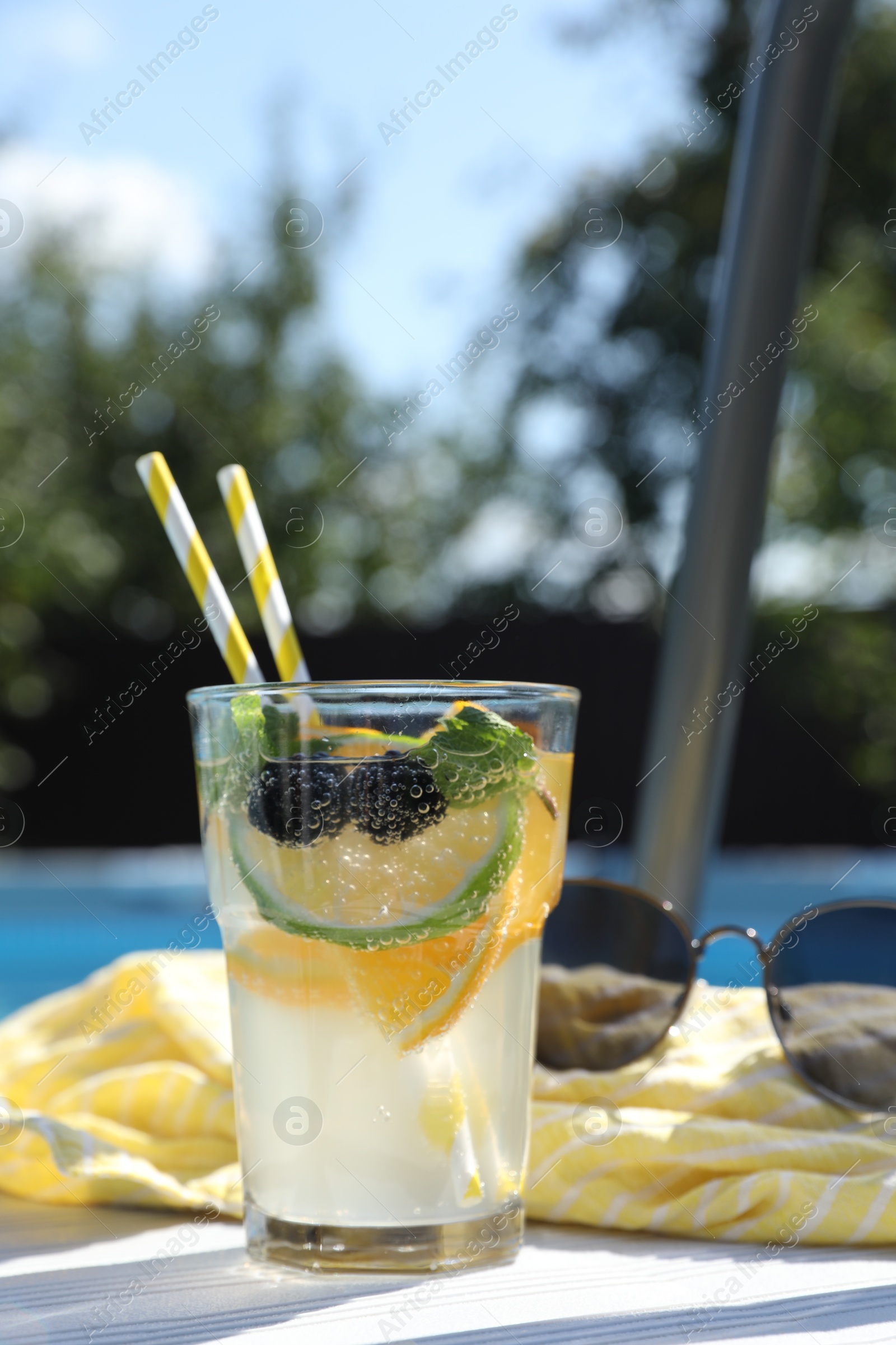 Photo of Tasty cocktail in glass and sunglasses near swimming pool outdoors