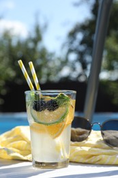 Photo of Tasty cocktail in glass and sunglasses near swimming pool outdoors