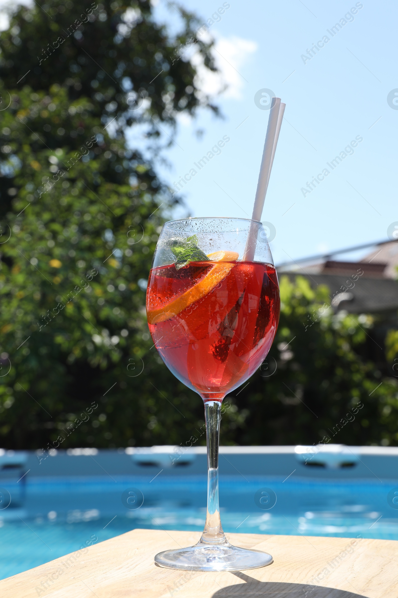 Photo of Tasty cocktail in glass near swimming pool outdoors