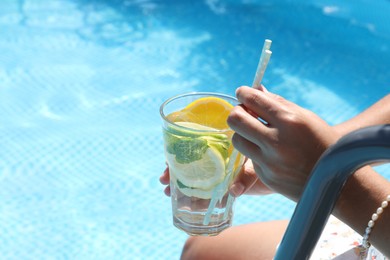 Photo of Woman holding tasty cocktail in glass near swimming pool outdoors, closeup