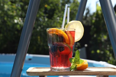 Photo of Tasty cocktail in glass near swimming pool outdoors