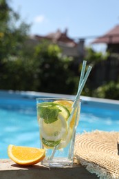 Photo of Tasty cocktail in glass near swimming pool outdoors