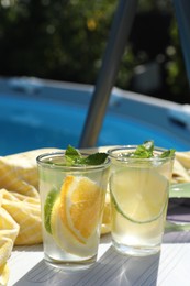 Photo of Tasty cocktail in glasses near swimming pool outdoors