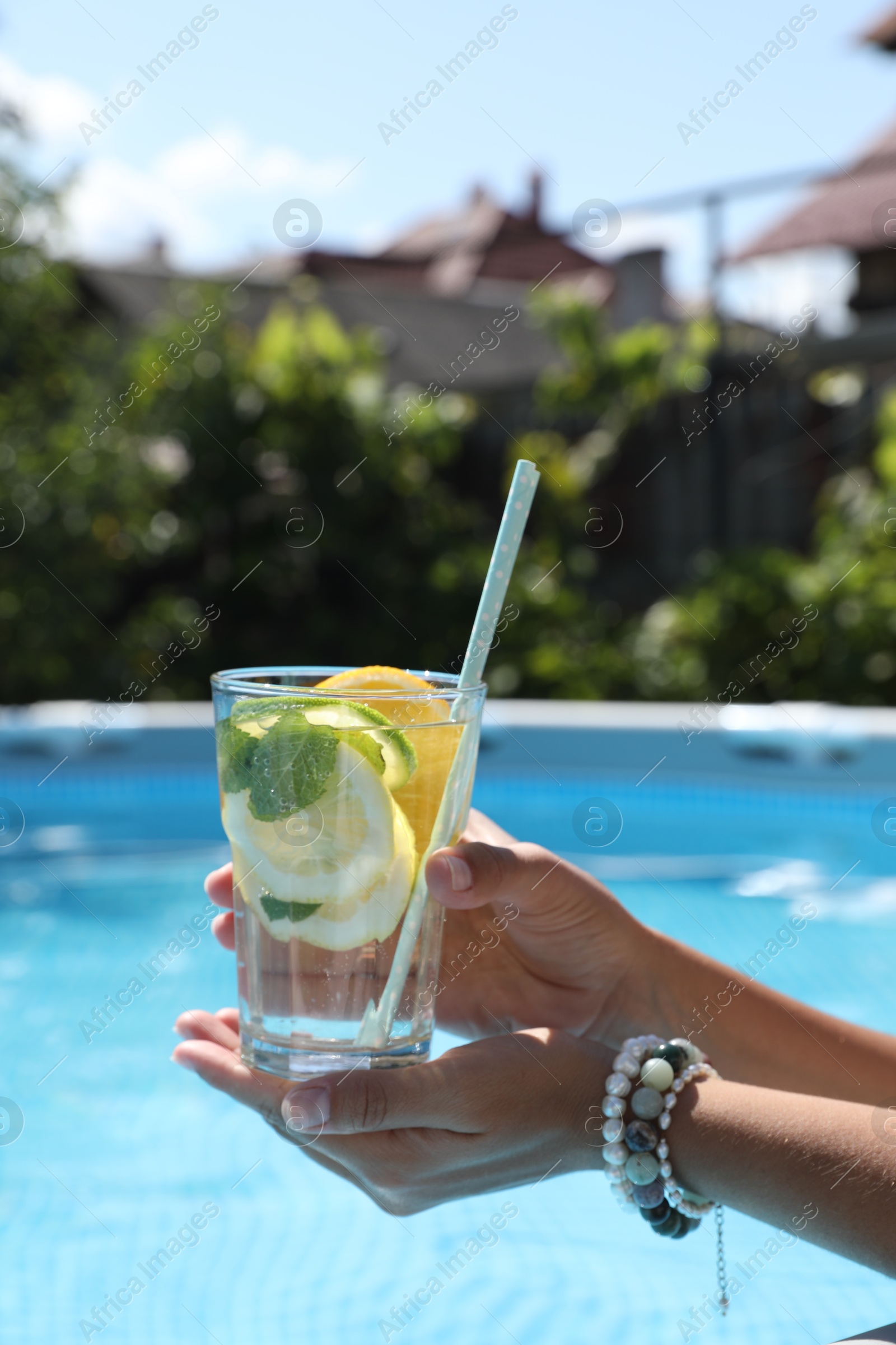 Photo of Woman holding tasty cocktail in glass near swimming pool outdoors, closeup