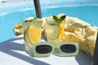 Tasty cocktail in glasses and sunglasses near swimming pool outdoors