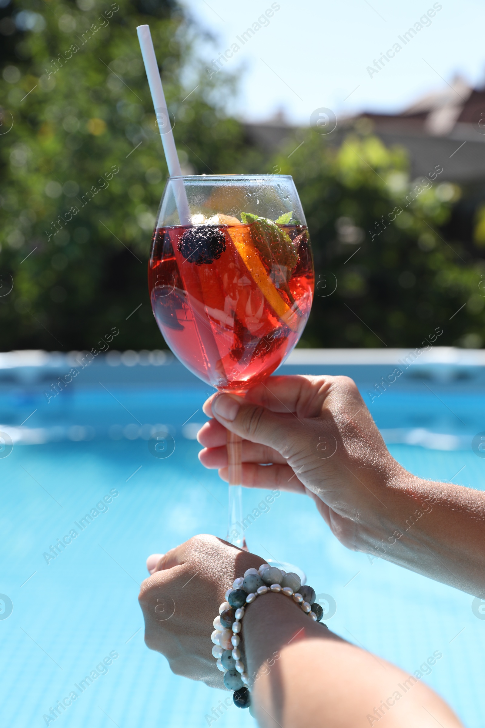 Photo of Woman holding tasty cocktail in glass near swimming pool outdoors, closeup