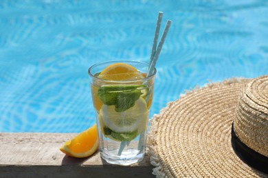 Photo of Tasty cocktail in glass and straw hat near swimming pool outdoors