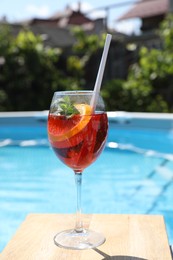 Photo of Tasty cocktail in glass near swimming pool outdoors