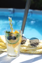 Photo of Tasty cocktail in glass and sunglasses near swimming pool outdoors