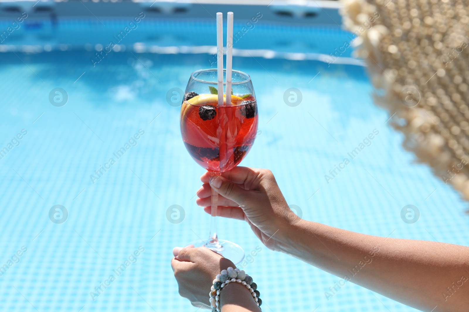 Photo of Woman holding tasty cocktail in glass near swimming pool outdoors, closeup