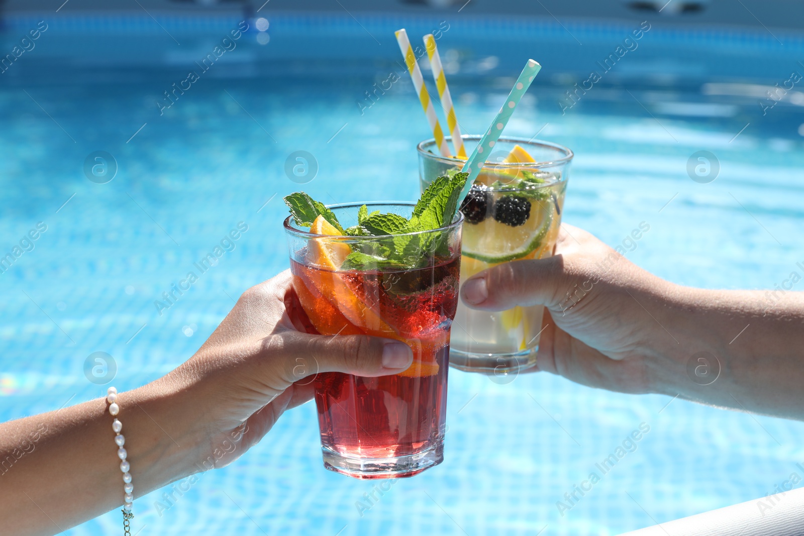 Photo of Women holding tasty cocktail in glass near swimming pool outdoors, closeup