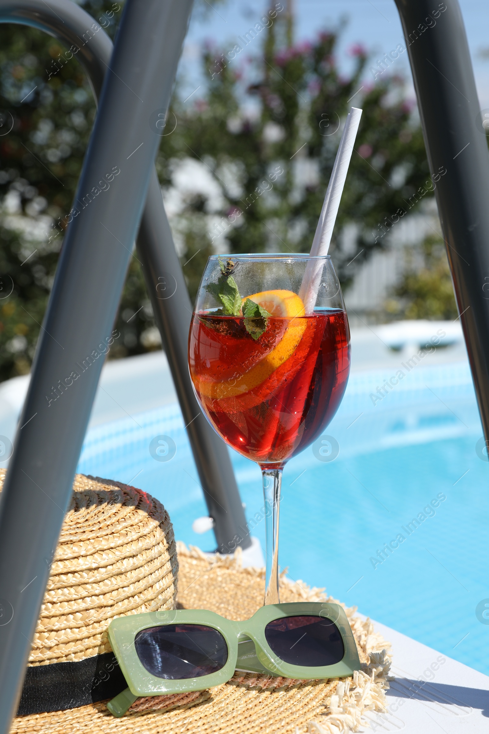 Photo of Tasty cocktail in glass and sunglasses near swimming pool outdoors